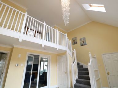 A hallway with white staircase and grey carpet two doors and a balcony with white railing at Drifters in Winterton-On-Sea