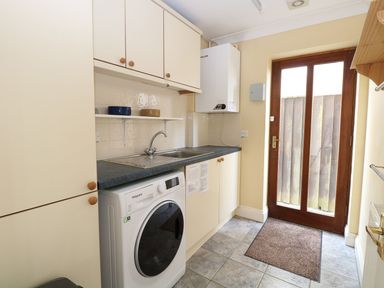 A utility room with washing machine, sink, cabinets, and a wooden door at Drifters in Winterton-On-Sea