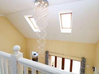 An interior view of a room with two skylight windows a modern hanging light fixture white stair railing yellow walls and a doorway to a bedroom at Drifters Winterton-On-Sea