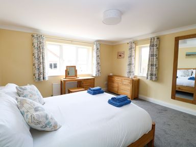 A bedroom with a bed, dressing table, chest of drawers, mirror, and windows with curtains at Drifters in Winterton-On-Sea