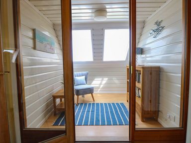 A small room with a blue striped rug a blue chair a wooden side table a wooden bookshelf and two skylight windows at Drifters in Winterton-On-Sea