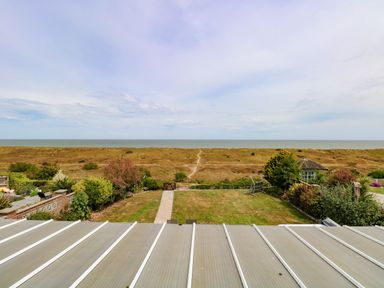 A garden with a lawn and path leading to a gate with dunes and the sea in the background at Drifters in Winterton-On-Sea