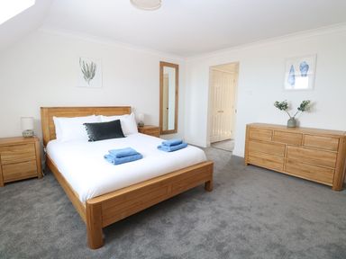 A bedroom with a wooden bed a dresser two nightstands and a full length mirror at Drifters in Winterton-On-Sea