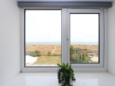 A window with a view of a garden and dunes beyond at Drifters in Winterton-On-Sea