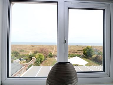 View through a window overlooking a garden with plants and a lawn beyond to sand dunes and the sea at Drifters Winterton-On-Sea
