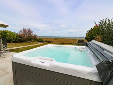 An outdoor hot tub on a patio with garden chairs near a grassy area and a view of the sea at Drifters in Winterton-On-Sea