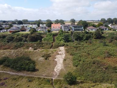 A row of houses behind a green hillside and a sandy path at Drifters in Winterton-On-Sea