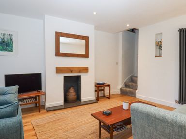 A living room with a fireplace a wooden coffee table a television and a staircase at The Cottage on The Square in Chagford