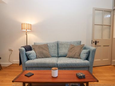 A living room with a blue sofa pillows a wooden coffee table and a floor lamp at The Cottage on The Square in Chagford
