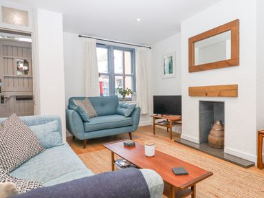 A living room with blue sofas a wooden coffee table a TV and a fireplace at The Cottage on The Square in Chagford