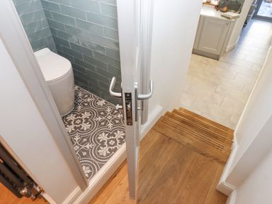 A small bathroom with patterned floor tiles and a toilet next to a hallway with wooden stairs and tiled floor at The Cottage on The Square in Chagford