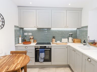 A kitchen with grey cabinets a wooden table an oven and a sink with green tile backsplash at The Cottage on The Square in Chagford