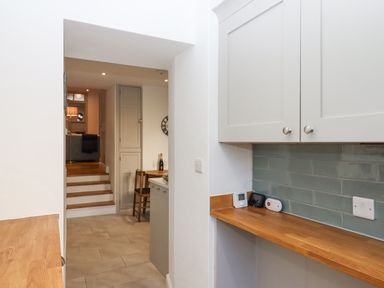 A kitchen area with wooden countertops white cabinets and green subway tile backsplash at The Cottage on The Square in Chagford