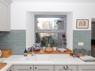 A kitchen sink under a window with plants on the windowsill and tiled backsplash at The Cottage on The Square in Chagford
