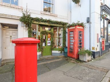 Shopfront of The Dartmoor Shepherd with green door and window surrounded by garlands red telephone box and red post box on the pavement