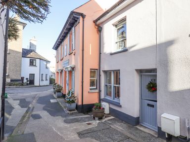 A narrow street with houses on either side including a building with orange walls and a white building with a blue door at The Cottage on The Square in Chagford