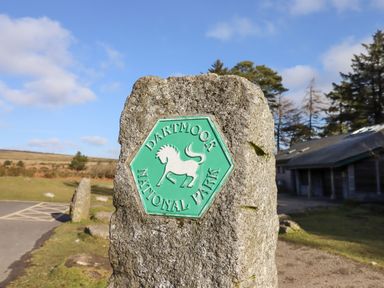 A stone marker with a green plaque reading Dartmoor National Park near a building and trees at The Cottage on The Square in Chagford