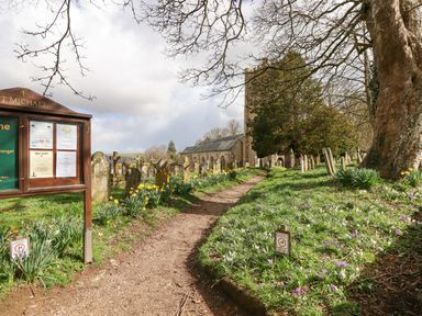 A graveyard with tombstones flowers and a church building in the background at The Cottage on The Square in Chagford