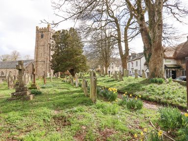 A churchyard with gravestones trees and daffodils near buildings at The Cottage on The Square in Chagford