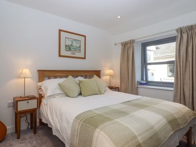 A bedroom with a wooden bed frame bedside tables lamps and a window with curtains at The Cottage on The Square in Chagford