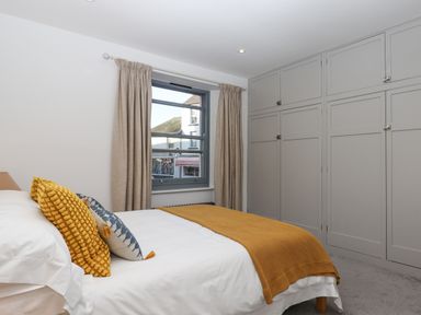 A bedroom with a bed covered in white and mustard bedding next to a window and built in cupboards at The Cottage on The Square in Chagford