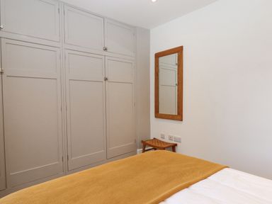 A bedroom with built-in closets a wall mirror and a small wooden stool at The Cottage on The Square in Chagford