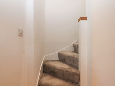 A carpeted staircase with a white wall and a light switch at The Cottage on The Square in Chagford
