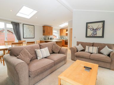 A living room with two brown sofas a wooden coffee table and a dining table with chairs at Highfield Lodge in Kirkstone 30 Limefitt Park near Troutbeck