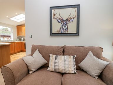A brown couch with three pillows and a painting of a deer on the wall in a living room at Highfield Lodge in Kirkstone 30 Limefitt Park near Troutbeck