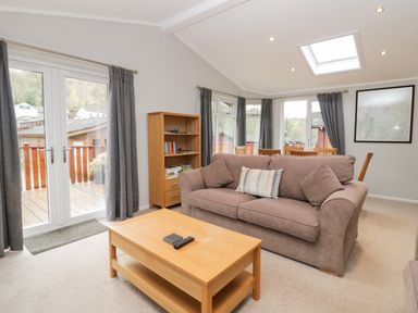 A living room with a brown sofa wooden coffee table bookshelf and dining table at Highfield Lodge Kirkstone 30 Limefitt Park near Troutbeck