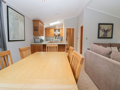 A dining area with wooden table and chairs next to a kitchen with wooden cabinets and appliances at Highfield Lodge Kirkstone 30 Limefitt Park near Troutbeck