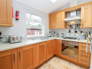 A kitchen with wooden cabinets a gas stove a toaster and a window at Highfield Lodge Kirkstone 30 Limefitt Park near Troutbeck