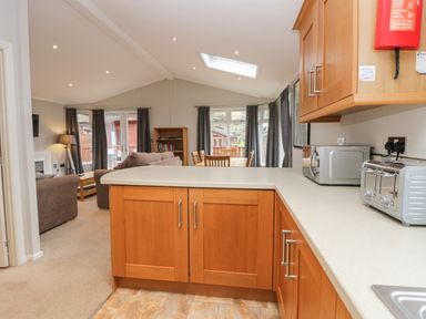 A kitchen with wooden cabinets and appliances opening to a living and dining area with furniture and windows at Highfield Lodge Kirkstone 30 Limefitt Park near Troutbeck