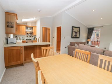 An open plan kitchen and living area with wooden dining table chairs grey sofas and a wall painting at Highfield Lodge Kirkstone 30 Limefitt Park near Troutbeck