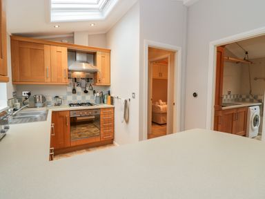 A kitchen with wooden cabinets a built in oven a washing machine in a utility room and a bedroom visible through doorways at Highfield Lodge Kirkstone 30 Limefitt Park near Troutbeck