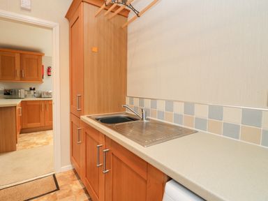 A kitchen area with wooden cabinets a stainless steel sink and tiled backsplash at Highfield Lodge Kirkstone 30 Limefitt Park near Troutbeck