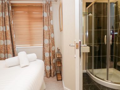 A bedroom with a bed, rolled white towels, window with blinds and curtains, and an adjacent bathroom with a corner shower at Highfield Lodge Kirkstone 30 Limefitt Park near Troutbeck