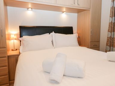 A bedroom with a double bed white pillows and rolled towels wooden cabinets and a small lamp at Highfield Lodge Kirkstone 30 Limefitt Park near Troutbeck