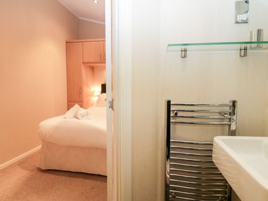 A bedroom with a bed and folded towels next to a bathroom with a towel rack and sink at Highfield Lodge Kirkstone 30 Limefitt Park near Troutbeck
