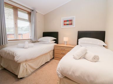 A bedroom with two single beds separated by a wooden nightstand with a lamp and a window with blinds and curtains at Highfield Lodge Kirkstone 30 Limefitt Park near Troutbeck