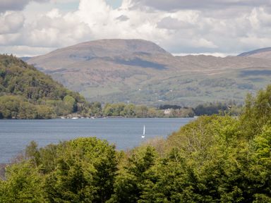 A lake with a sailboat surrounded by trees and hills at Highfield Lodge Kirkstone 30 Limefitt Park near Troutbeck