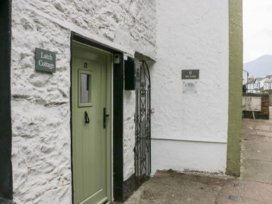 A green door numbered 12 next to a white wall with a sign reading Latch Cottage and an iron gate at Latch Cottage in Keswick