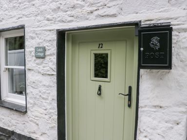 A green front door with the number 12 a black mailbox and window on a white stone wall at Latch Cottage in Keswick