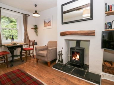 A living room with a wood stove fire armchair dining table and chairs with cushions at Latch Cottage in Keswick