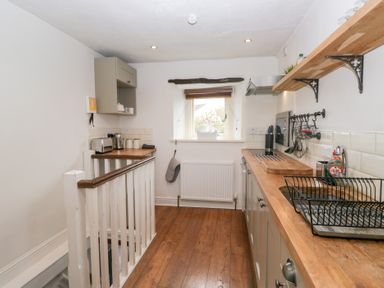 A narrow kitchen with wooden counters and floor with a window at the end at Latch Cottage in Keswick