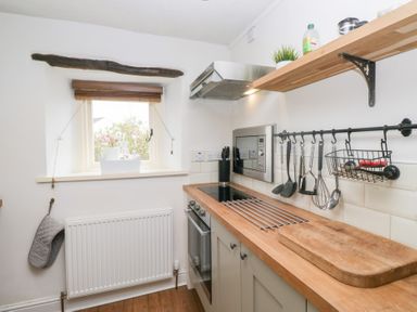 A small kitchen with a wooden countertop a cutting board hanging utensils an oven and a window with a view at Latch Cottage in Keswick