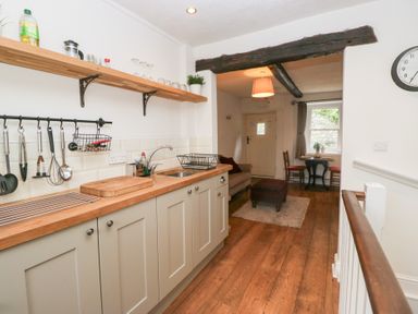 A kitchen with wooden countertop and utensils hanging on the wall leading to a sitting area with a table chairs and a door at Latch Cottage in Keswick