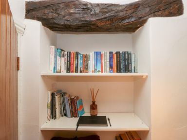 A small bookshelf with books a notebook pen and a reed diffuser under a wooden beam at Latch Cottage in Keswick