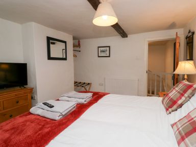 A bedroom with a bed with red and white pillows and blankets a wooden dresser with a TV and a wall mirror at Latch Cottage in Keswick