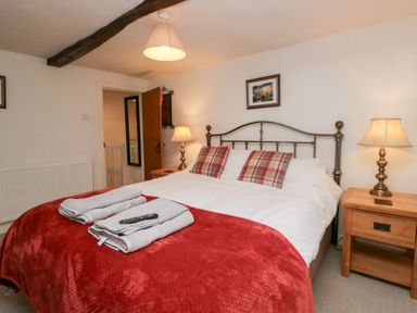A bedroom with a double bed with red and white beddings and plaid pillows two wooden bedside tables with lamps and a wall painting at Latch Cottage in Keswick